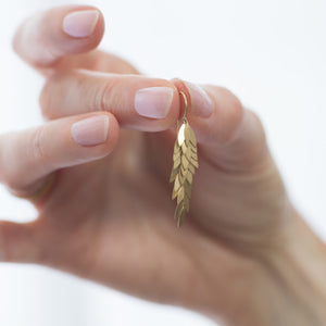 Detail view of model holding a Golden Leaf Earring by Sia Taylor in her right hand.