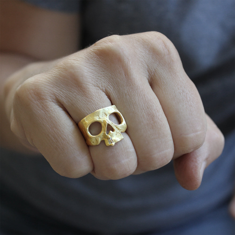 Model making fist with right hand, wearing 18k yellow gold Skull Ring with Diamond Snaggletooth by Polly Wales.